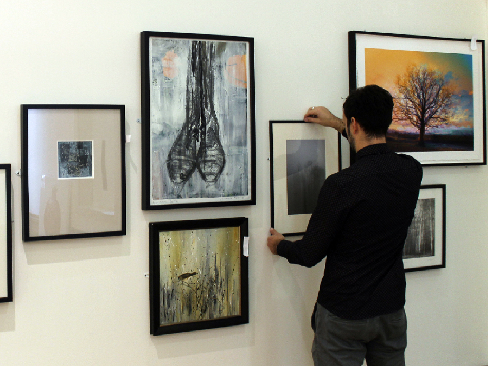 Staff member hanging artwork on the walls of The Front Room Gallery.