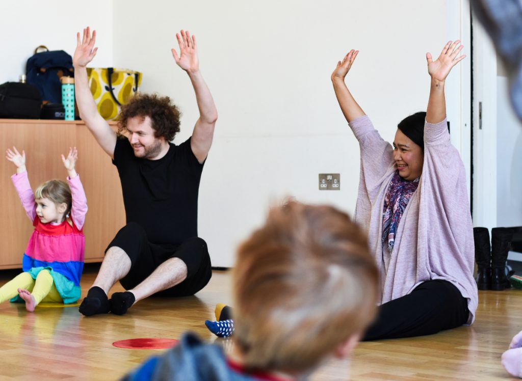 Adults and children sitting on the floor with their arms in the air