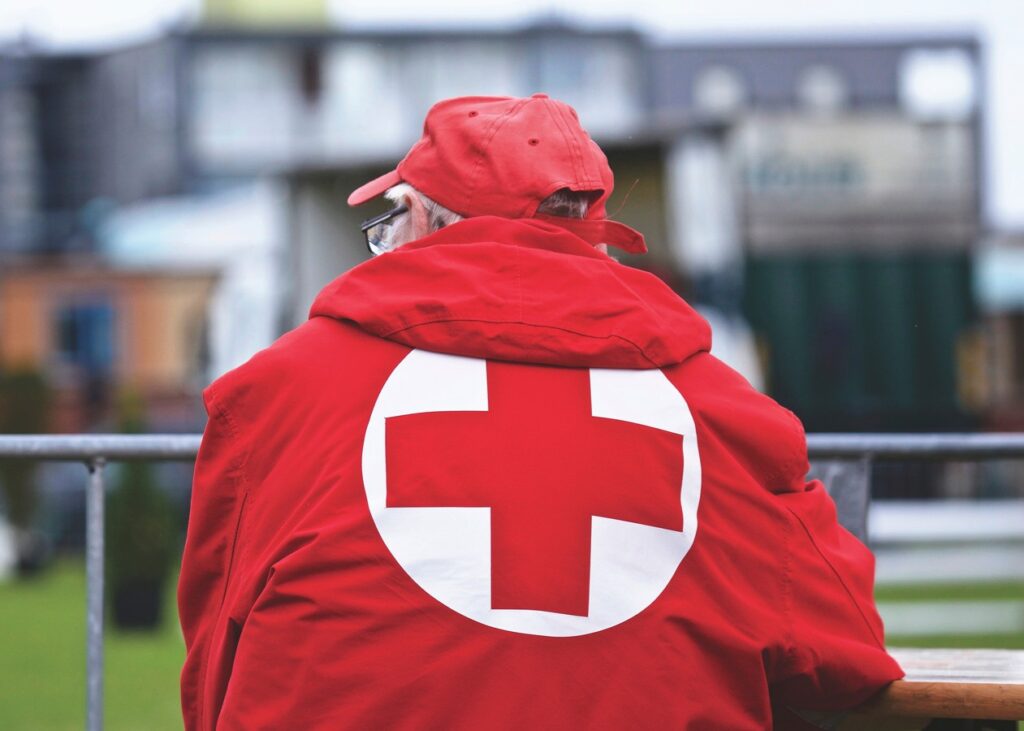 Man wearing a British Red Cross coat with his back to the camera