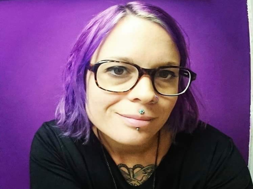 Girl with purple hair taking a selfie in front of a purple background