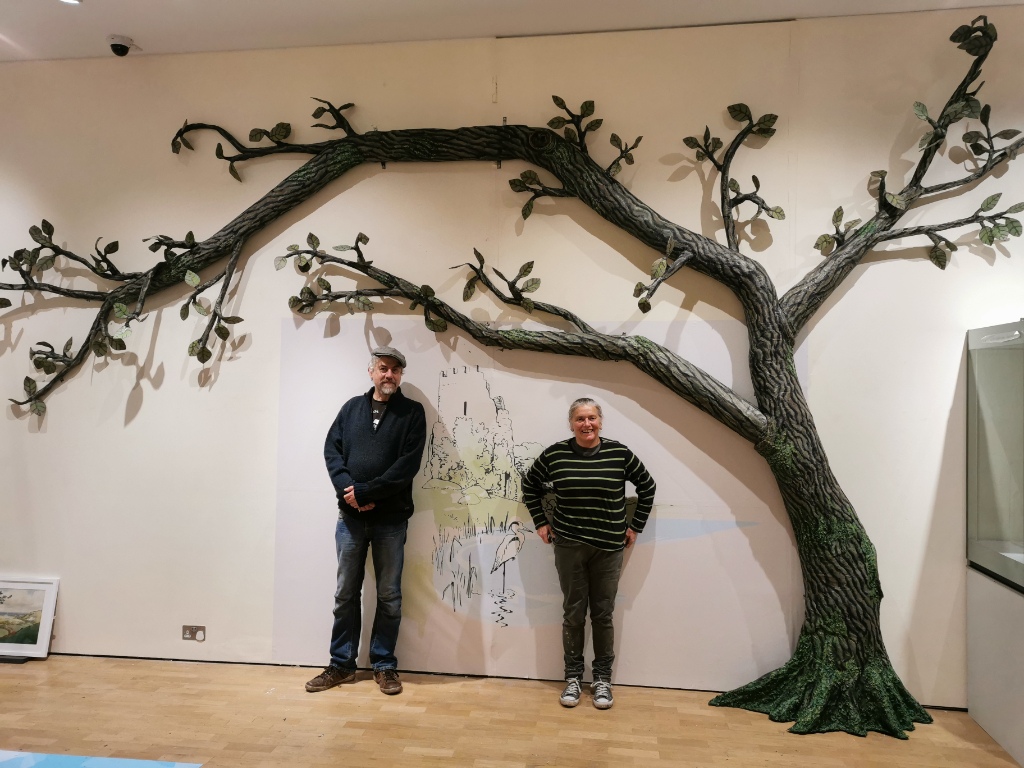 2 artists standing underneath a tree sculpture 
