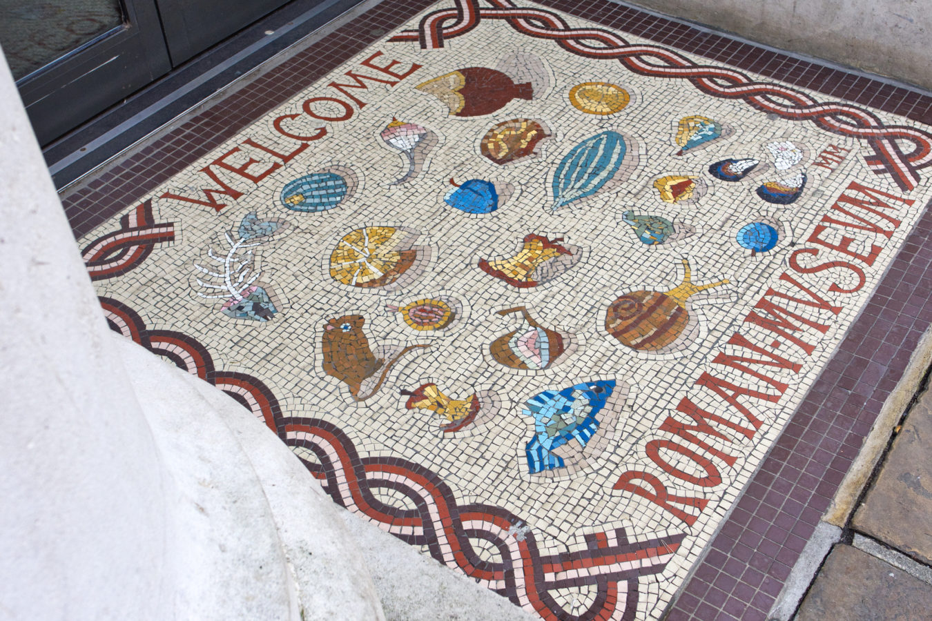 A mosaic replica outside the Roman Museum entrance stating 'Welcome Roman Museum'