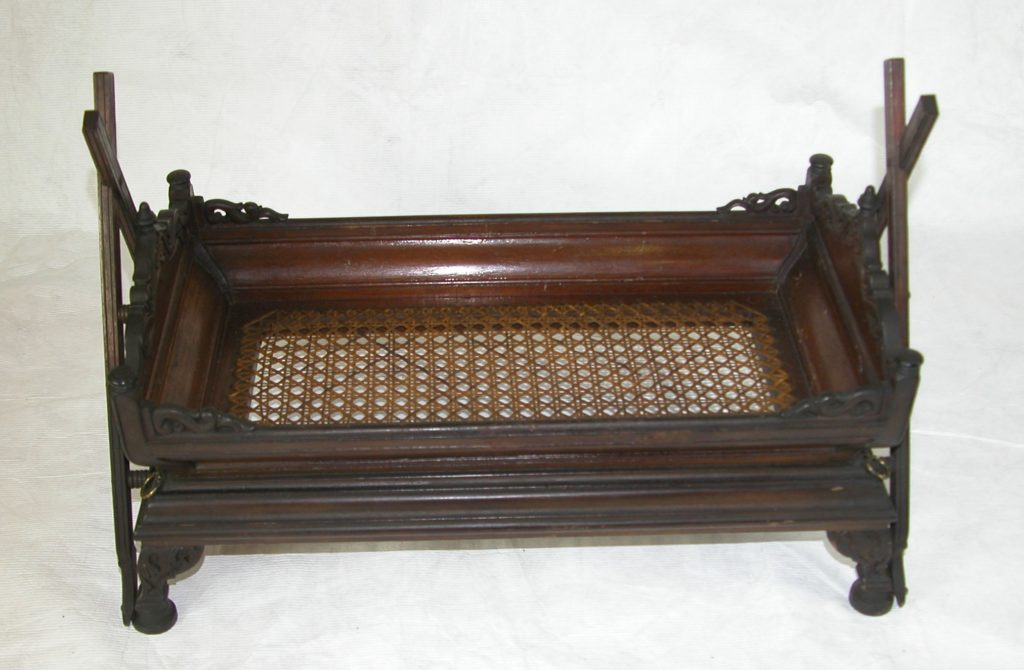 Carved wooden cradle with sides and bottom with cane, resting on four carved legs