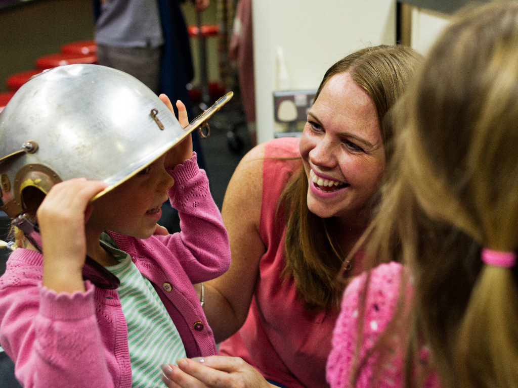 Child trying on a Roman soldier helmet as mother laughs