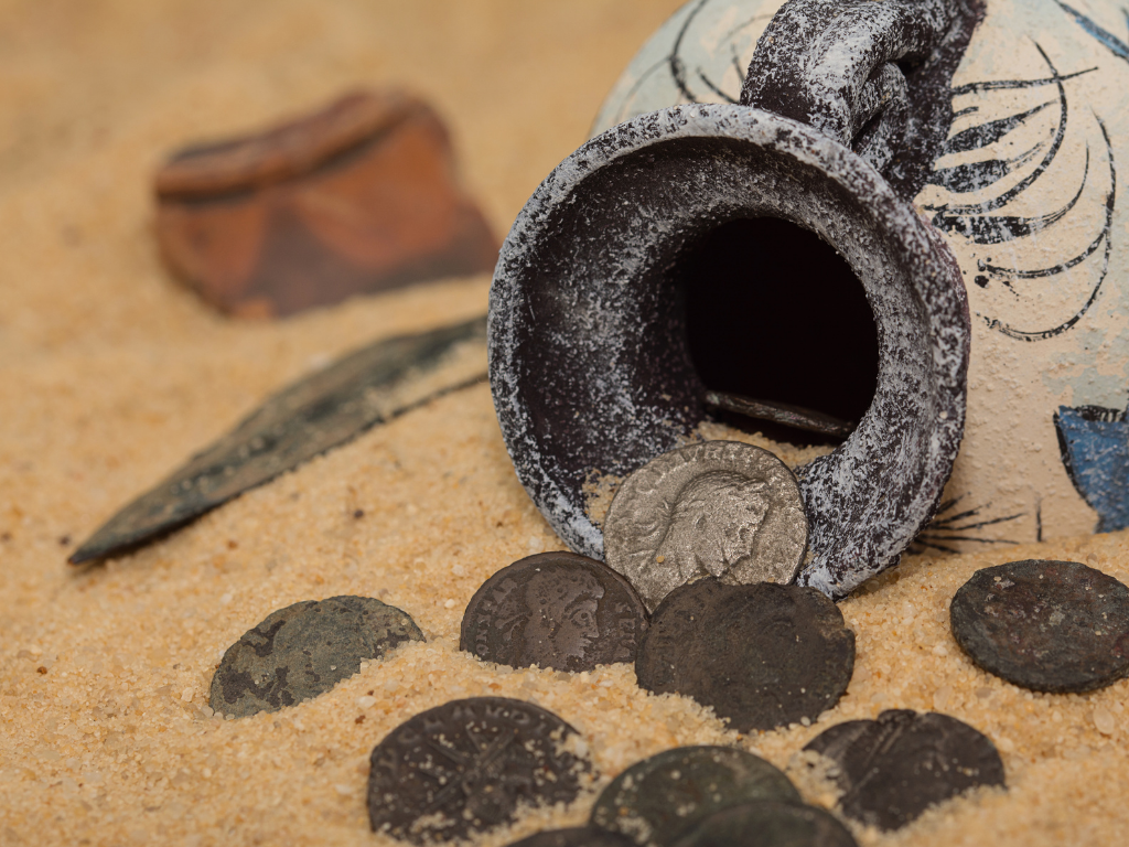 Roman coins spilling out of a Roman pot in sand