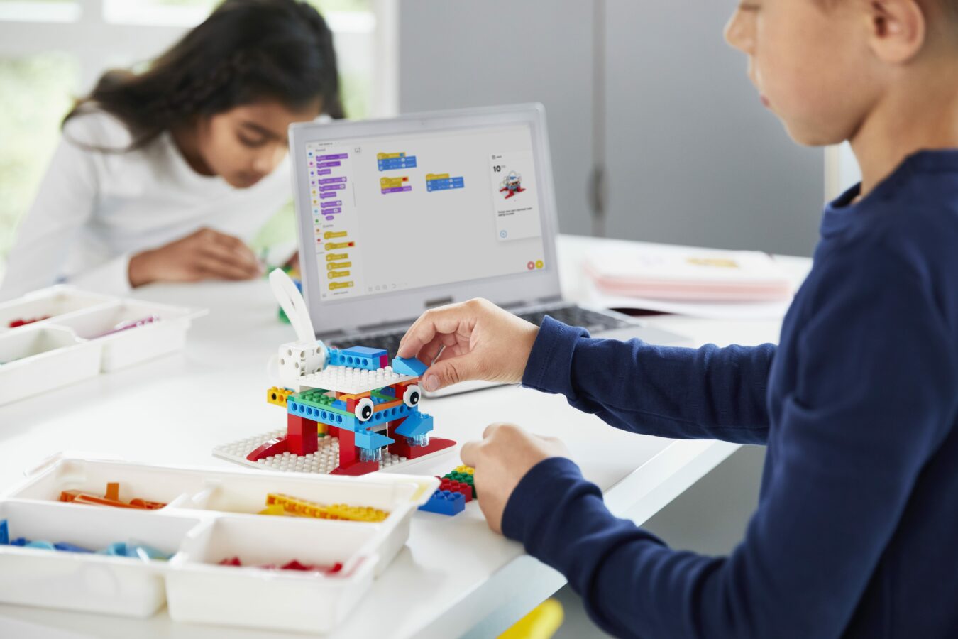 children using a tablet and colourful lego bricks to create robots with coding and motors 