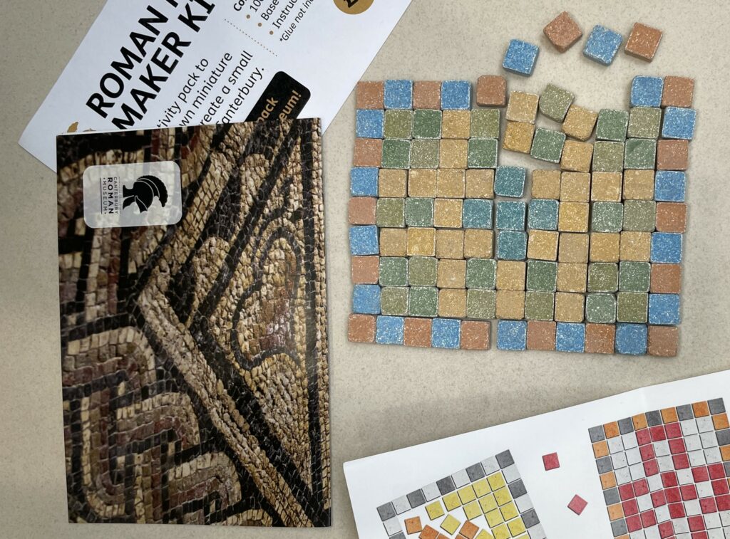 a craft kit with a mosaic made from colourful square tiles next to a photograph of a roman mosaic and some instructional material